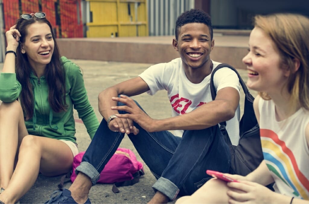 3 students, sitting down, laughing and smiling.