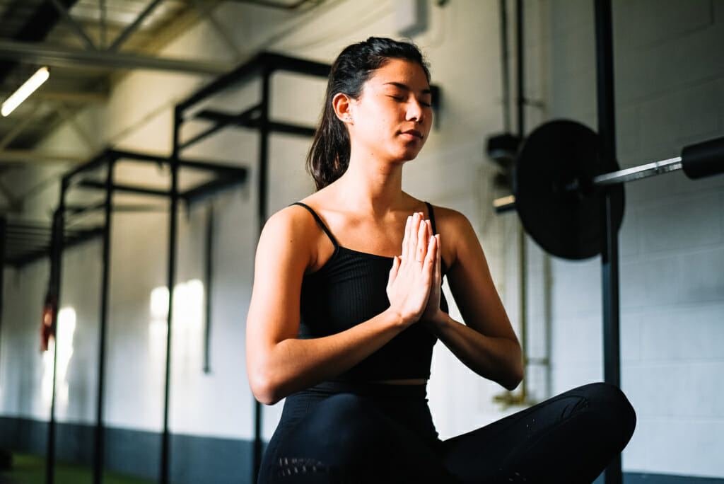 female sat on floor in a gym, practicing yoga.